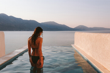 A young woman on a luxury vacation. Back view of a woman in a bikini staying in the infinity...