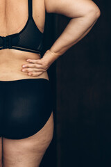 Fototapeta premium Woman with back pain in black underwear. Capturing a moment of discomfort, a woman clasps her lower back.