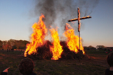 Das Osterfeuer ist angezündet: Ein Brauch zum religiösen Fest mit flammenden Kreuz und Menschen auf dem Acker.