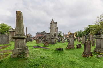 Fototapeta na wymiar The lush greenery of Stirling's iconic cemetery envelopes time-worn gravestones, with the imposing medieval tower of the Church of the Holy Rude