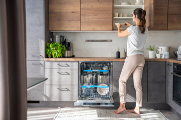 Woman removes clean ceramic dishes from the dishwasher. Household and useful technology concept.