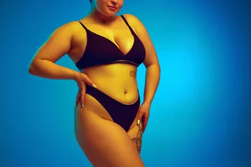 Schilderijen op glas Woman, model plus size in dark lingerie, showcasing natural body curves in yellow neon light against blue studio background. Concept of natural beauty, femininity, body positivity, dieting, fitness. © Lustre