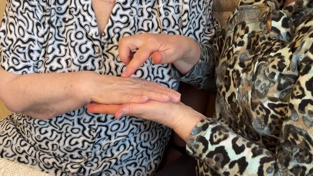 A woman holds the old wrinkled hands of an elderly woman and gives her an acupressure of the hands. She calms an elderly grandmother during times of stress. Close-up