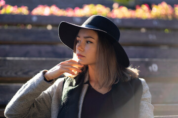 A lonely girl in a black hat sits in on a summer theater bench