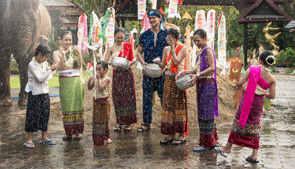 Group of Thai women, man and children in colorful traditional Thai clothing holding silverware bowl...