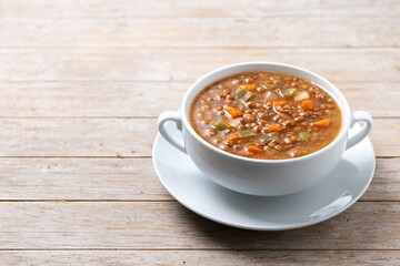 Lentil soup with vegetables in bowl on wooden table. Copy space