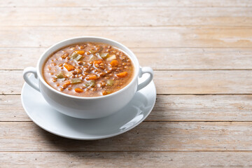 Lentil soup with vegetables in bowl on wooden table. Copy space
