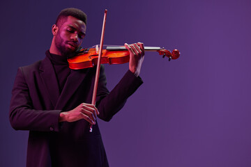 Man in black suit playing violin on purple background in elegant musical performance concept