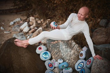 Young hairless girl with alopecia in white futuristic costume pensively examines stone with eye at...