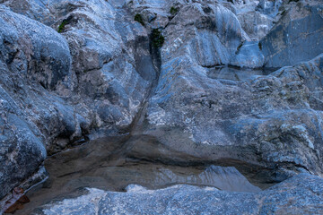 Fototapeta na wymiar Small puddle in blue rock close up, dent in stone filled with water during blue hour