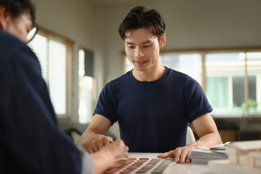 Smiling Asian male client choosing paint colors for renovation at office.