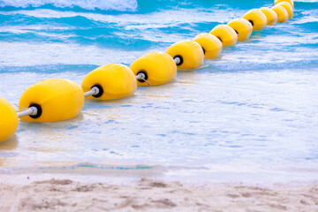 Yellow sea buoy. Ocean with floating buoys and rope dividers on the beach. Clear blue water and sandy beach. Sea background.
