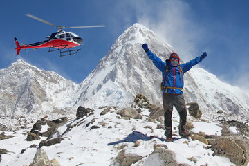 Hiker with open arms in the Himalayan mountains. Successful man with rescue helicopter. In the background the Pumori mountain in Himalaya, Nepal
