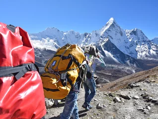 Fototapete Ama Dablam The adult sherpa porters carrying heavy backpacks and sacks in the Himalayas at Nepal, in the background the mountain of Ama Dablam