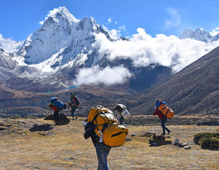 The adult sherpa porters carrying heavy backpacks and sacks in the Himalayas at Nepal, in the background the mountain of Ama Dablam