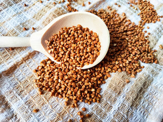 Buckwheat scattered on textured fabric and in a wooden spoon. Grits for cooking. Texture, background, copy space and place for text