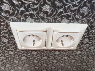 Two white European power outlets mounted on ornate wall. European Dual Socket on a Patterned Wall