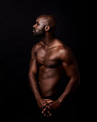 Fototapeta premium Black man, body and fitness on a dark background for dermatology and shadow or light with art deco or aesthetic. Bodybuilder, model or young person thinking in studio with shirtless abs and beauty
