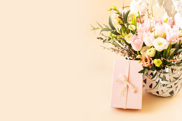 Beautiful bouquet of rose and tulips flowers and pink gift box on beige pastel background. Gift for...