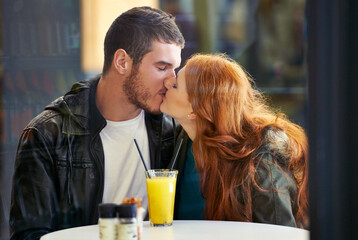 Couple, date and kiss with romance, cafe or restaurant with orange juice and happiness together. Man, woman and love for relationship, care and smile for flirting on break for relax or bonding