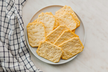 Golden Baked Crackers on plate on a White kitchen table. Top view.