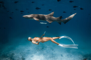 Woman in mask and fins swimming with nurse sharks in a tropical blue ocean in the Maldives.