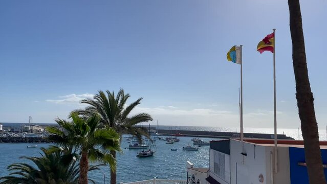 Flags of Canary Island and Spain waving next to the harbour of Arguineguin