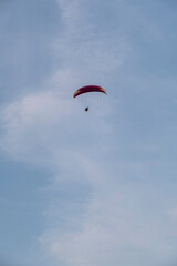A paraglider or paramotor flying over a beautiful blue sky with white clouds over the beach.Real Photo
