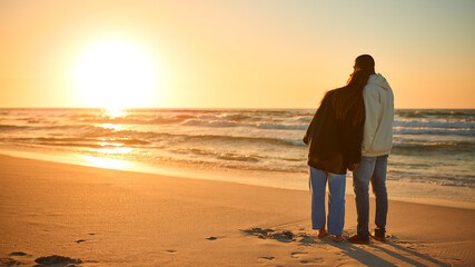 Rear View Of Casually Dressed Loving Young Couple Standing On Beach Shoreline Hugging At Sunrise