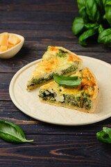 Unsweetened pastries, sliced quiche with spinach, oyster mushrooms, egg filling and cheese on a light ceramic dish on a dark wooden background. Spinach recipes. Snack pies.