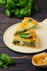 Unsweetened pastries, sliced quiche with spinach, oyster mushrooms, egg filling and cheese on a light ceramic dish on a dark wooden background. Spinach recipes. Snack pies.