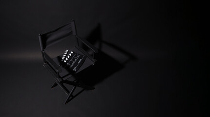 Black Director chair and clapper board with light an shadow on black background.Top view