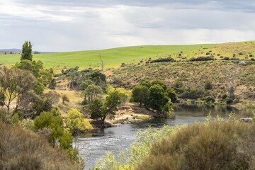 flowing river past farmland in summer, in the Tasmania wilderness. Lake with a Sandy beach and...