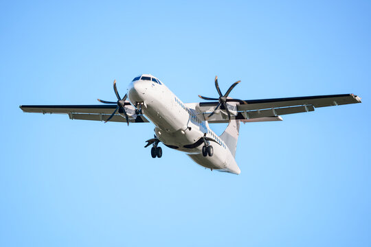 ATR 72 airplane, a twin-engine turboprop short-haul regional passenger aircraft. Landing airplane. Blue background. Clear sky.