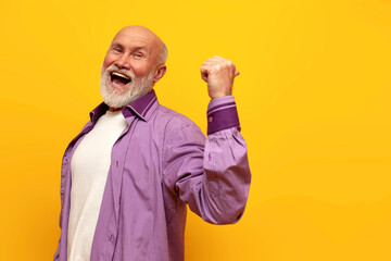 cheerful old bald grandfather in purple shirt shouts and points back on yellow isolated background