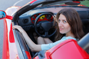 Portrait of young woman sitting behind wheel driving luxury roadster