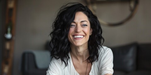 Portrait of a naturally smiling woman with dark curly hair, wearing casual clothing indoors. - obrazy, fototapety, plakaty
