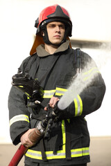 half-height portrait of fireman holds and adjust nozzle and fire hose spraying high pressure water