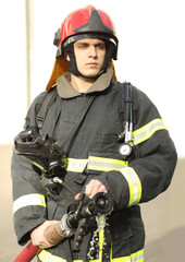 Obraz premium half-height portrait of fireman holds and adjust nozzle and fire hose spraying high pressure water, no jet