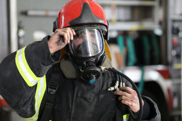 fireman wearing fire fighter turnouts and red helmet with breathing apparatus on background of fire...