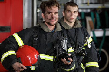 Obraz premium Two firefighters in protective suits standing against fire engine