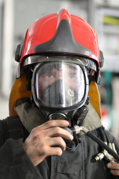 fireman wearing fire fighter turnouts and red helmet with breathing apparatus on background of fire truck, closeup