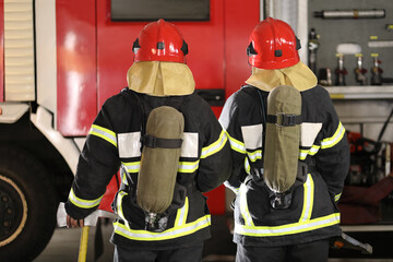 Fototapeta premium two firefighters in equipment and helmets against fire engine, back view