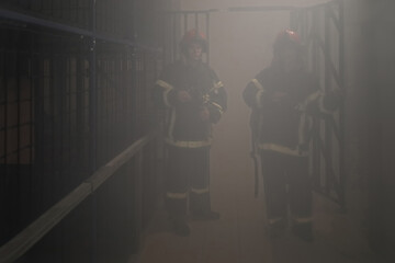 Fototapeta na wymiar Two firemen in smoky environment hold protective masks in smoke chamber
