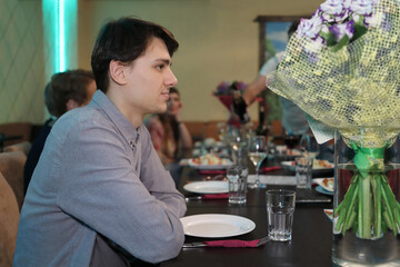 sitting guests invited to feast eat at table, young man in foreground waiting for food, empty plate