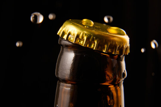 Close-up of opening glass beer bottle with golden cap with water droplets, condensation against black background. Concept of alcohol and non-alcohol drinks, refreshment. Poster, banner for ad
