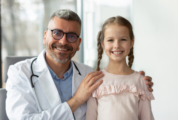 Portrait of happy male middle aged pediatrician and pretty child girl smiling at camera, kid at...