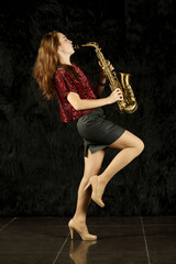 Young girl with closed eyes playing saxophone with raised leg in black room