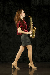 Young girl playing saxophone in black room