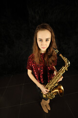 Portrait of young girl with saxophone in black room, top view